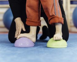 Flat feet correction exercise - Boy walking over spiked half balance massage balls  with support from physical therapist